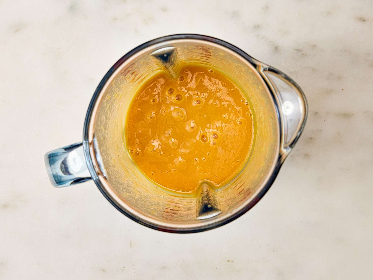 A blender containing a smooth orange mixture on a marble surface