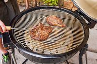 A person cooks meat inside the Weber 18201001 Summit Kamado E6 Charcoal Grill