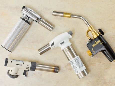 four kitchen torches on a beige surface