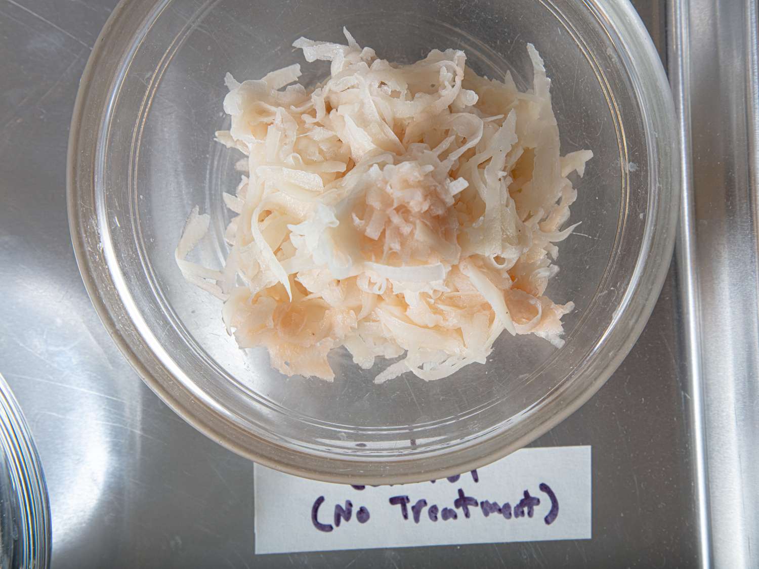 Bowl containing shredded potato labeled with no treatment shown on a steel surface