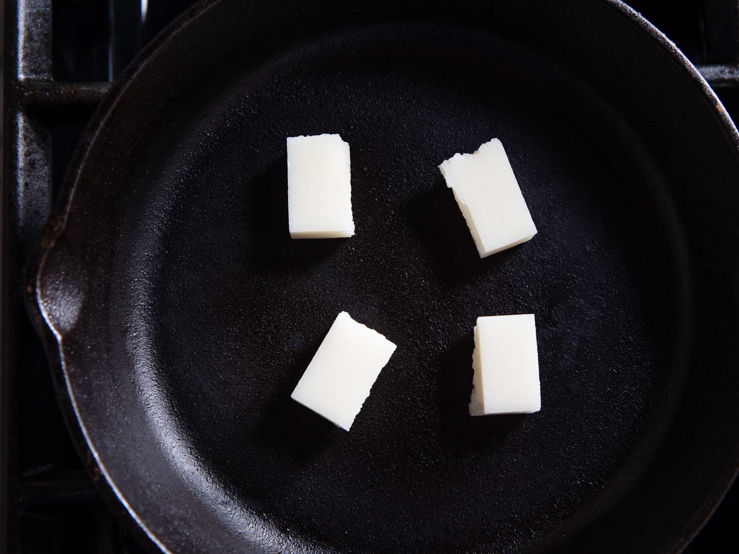 Four pieces of white mochi toasting in a cast iron skillet for Japanese ozoni.