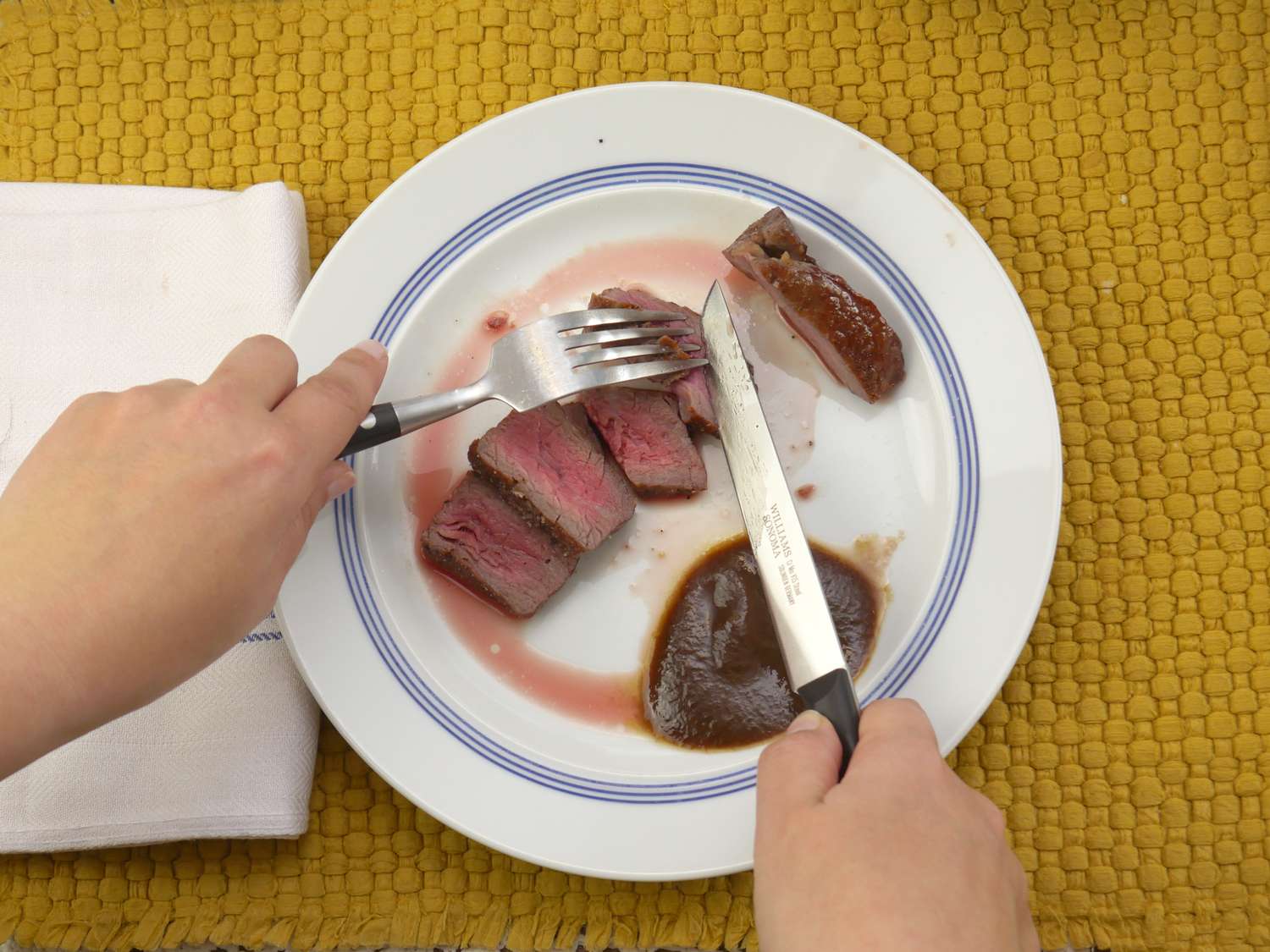 a person slicing steak with the williams sonoma steak knives