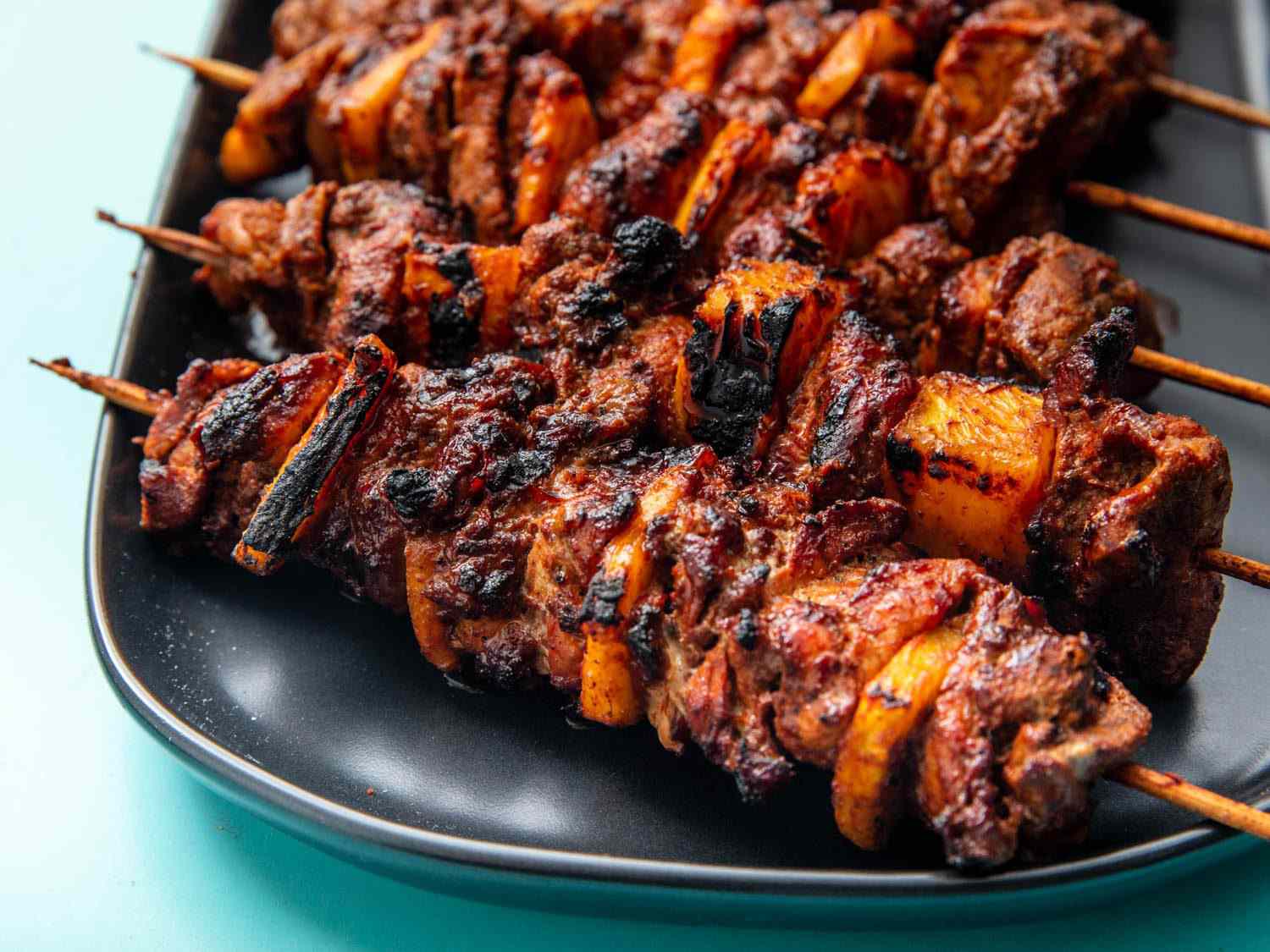 Closeup side view of al pastor skewers on a serving platter.