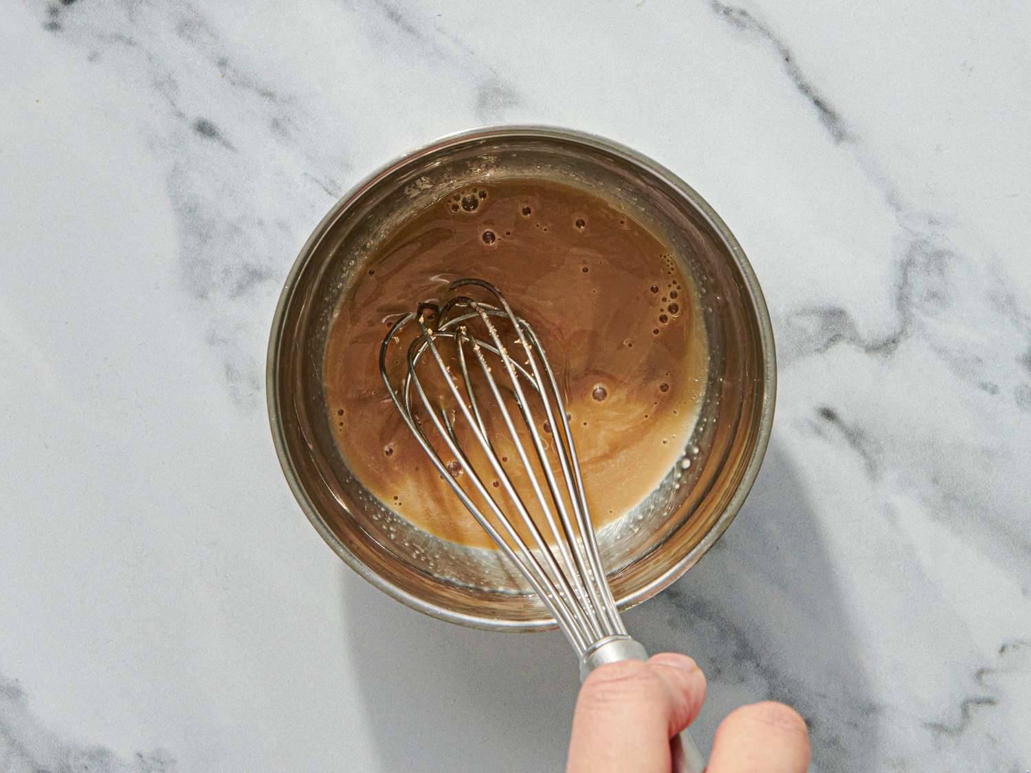 A hand whisking a liquid mixture in a metal bowl