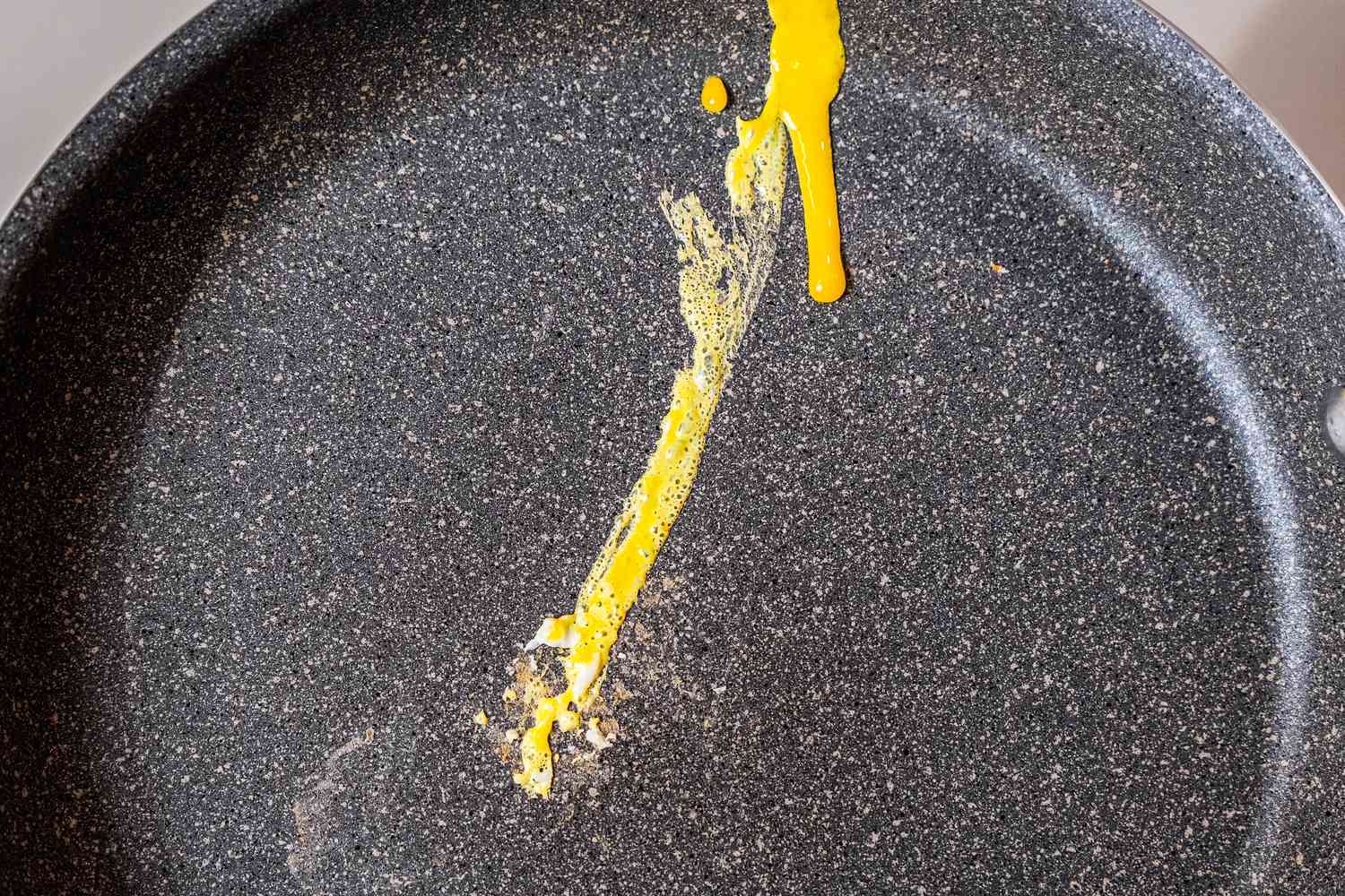 A closeup photo of yolk stuck to a gray nonstick pan