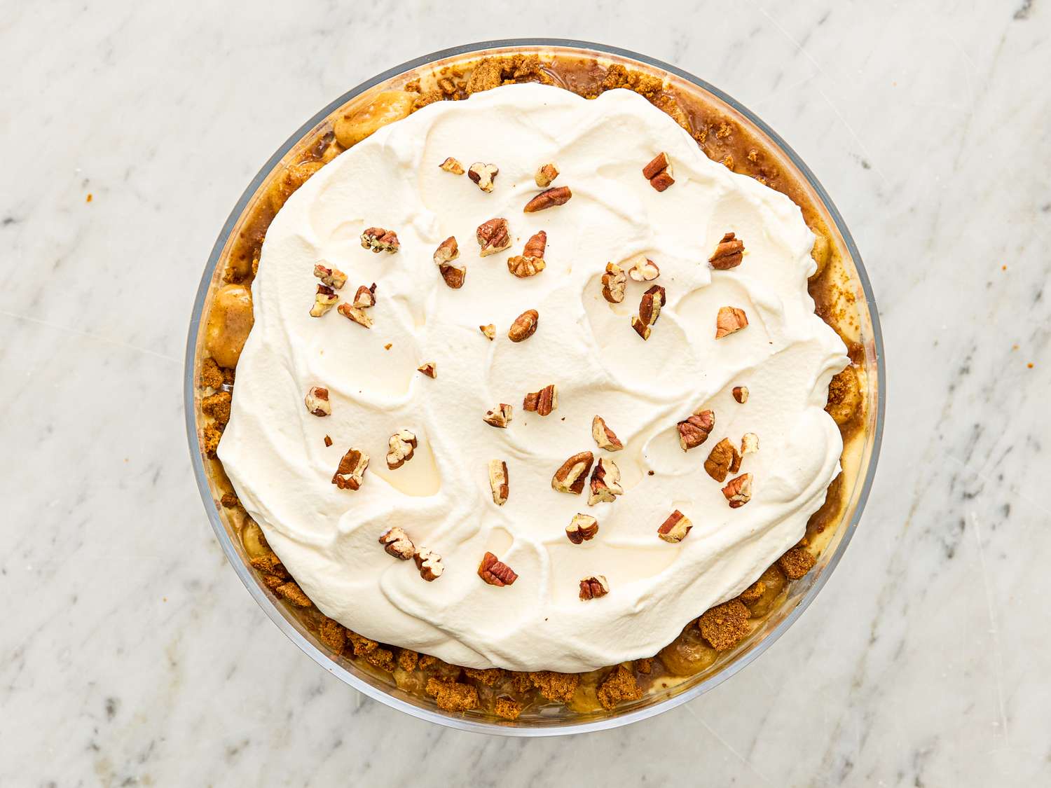A layered dessert topped with whipped cream and chopped nuts in a glass dish