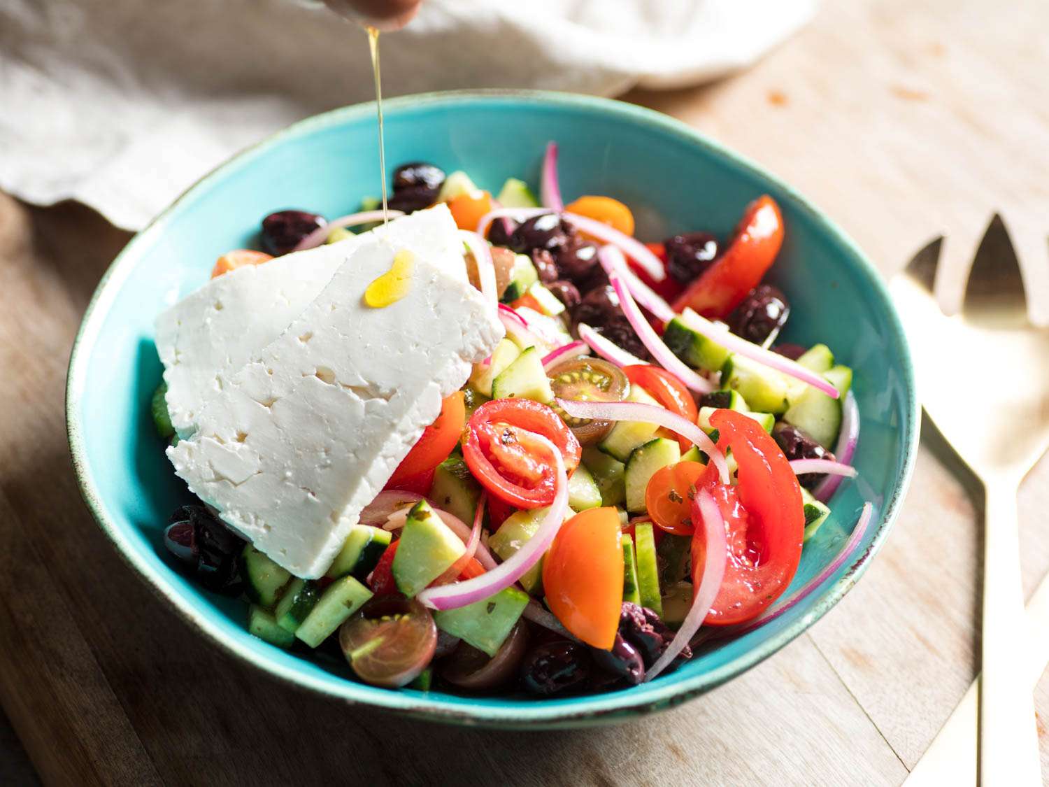 Drizzling olive oil over slabs of feta topping a Greek salad.
