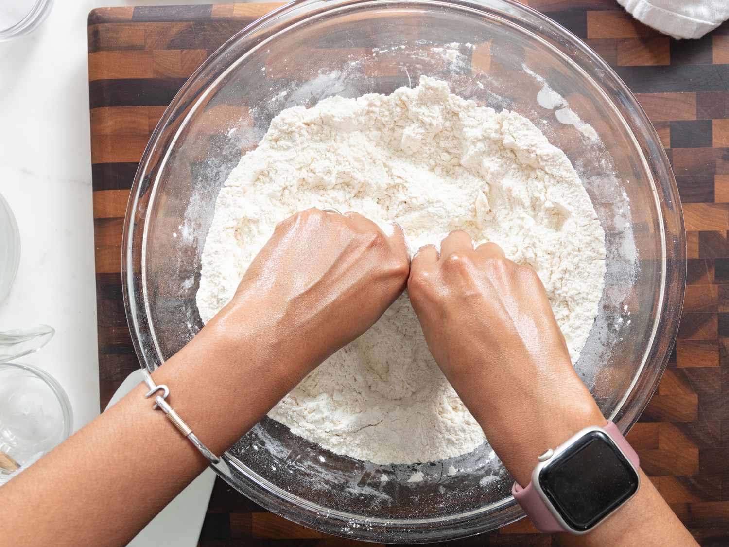 Hands in large glass bowl of dry dough ingredients on a wooden surface 