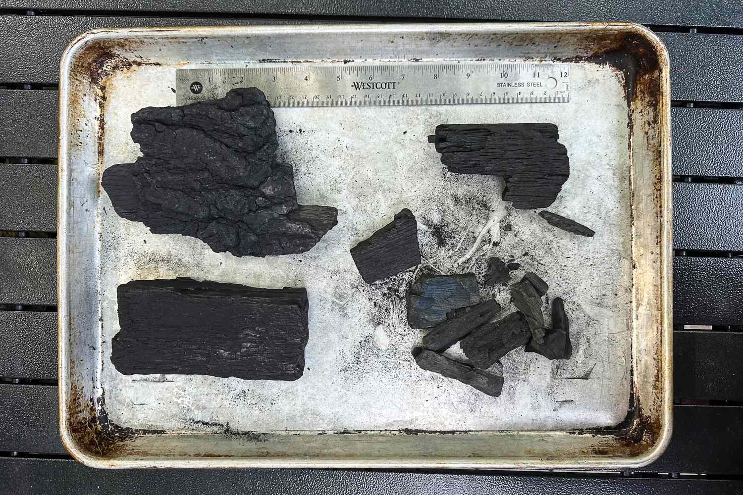 Pieces of charcoal arranged on a metal tray with a ruler