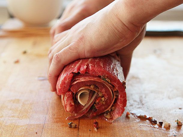 Hands rolling up a large piece of flank steak stuffed with cold cuts and cheese