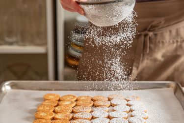 Sifting powdered sugar onto a tray of cookies