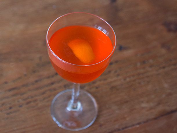 Intro to Aperol cocktail in small glass on wooden table.