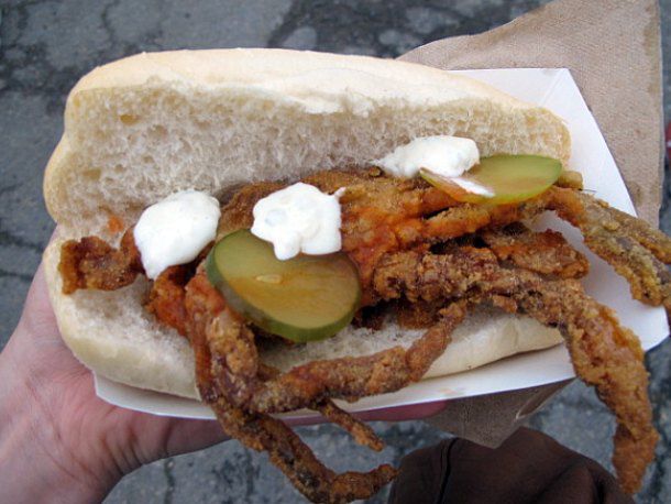 A deep fried soft-shell crab sandwich with pickle slices, mayo, and hot sauce on a split bun.