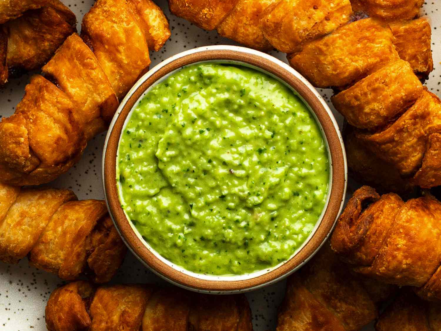 A close-up photo of a ceramic bowl holding guasacaca, surrounded by tequeÃ±os.