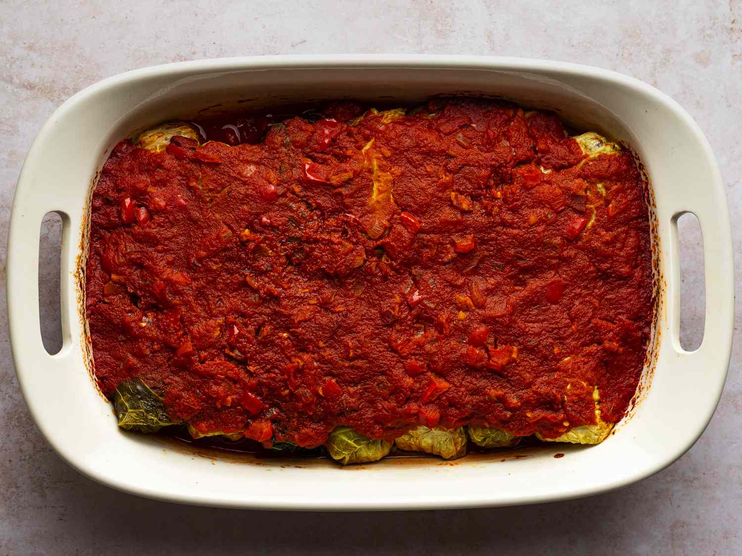 Cabbage rolls in baking dish after coming out of oven. The sauce is more visibly dehydrated and the color of the cabbage has changed from bright green to dull green.