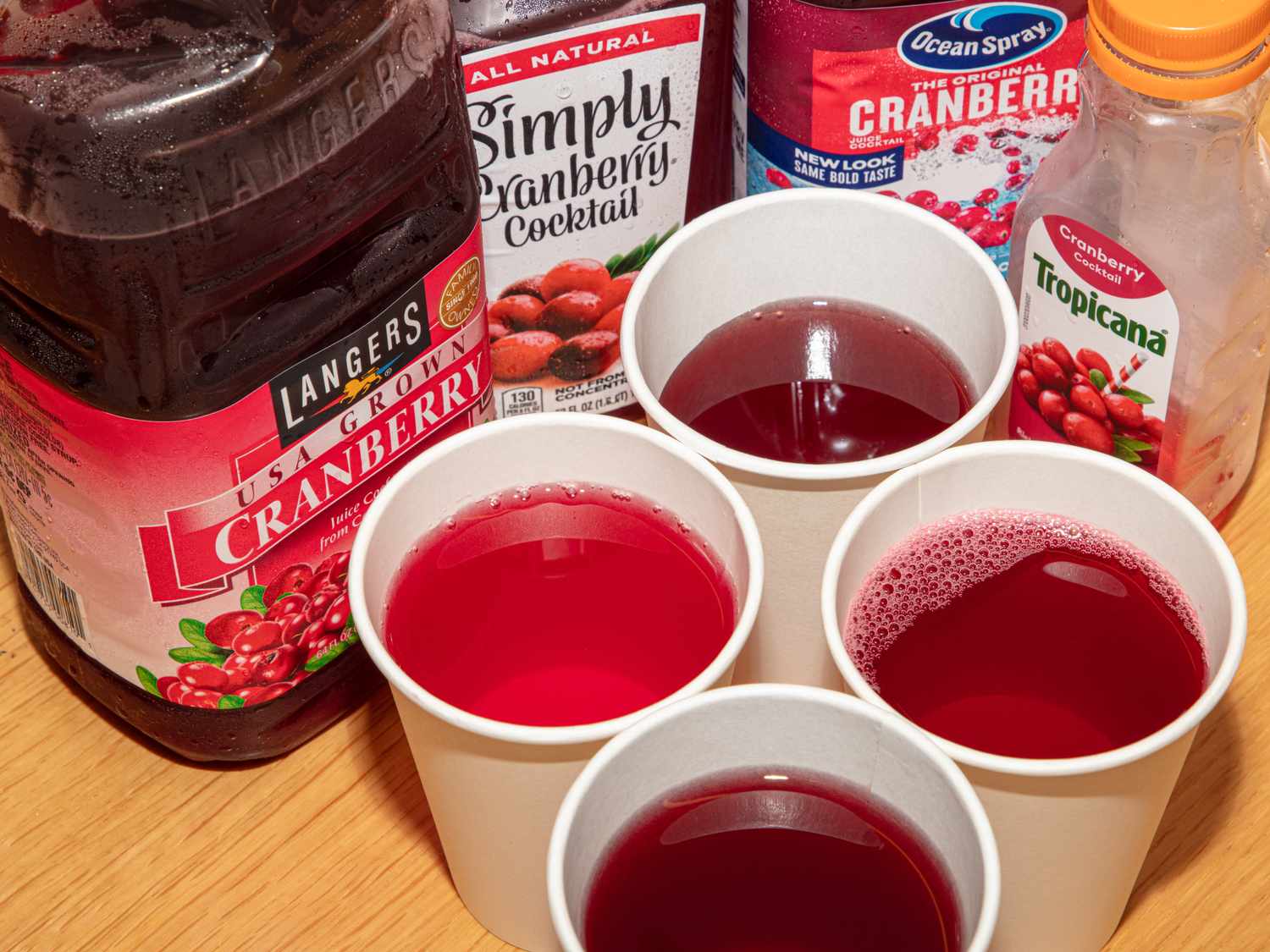 Various cranberry juice brands and four cups filled with cranberry juice on a table
