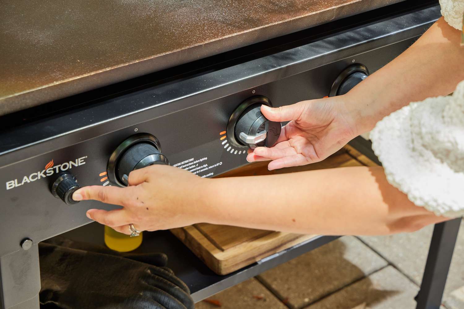 A person adjusts the temperature on the Blackstone 1554 Cooking 4 Burner Flat Top Gas Grill