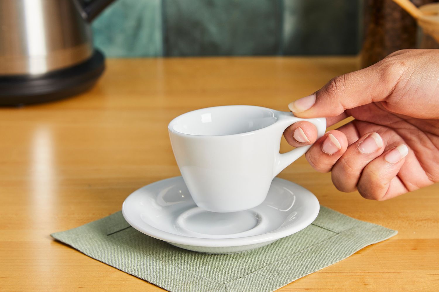 A person picking up a white coffee mug off of a saucer.