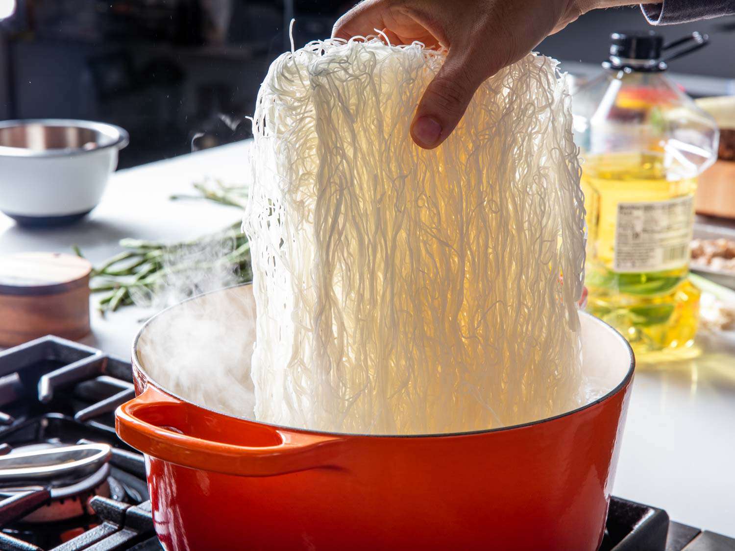 A large block of dried rice noodles is lowered into the boiling water.
