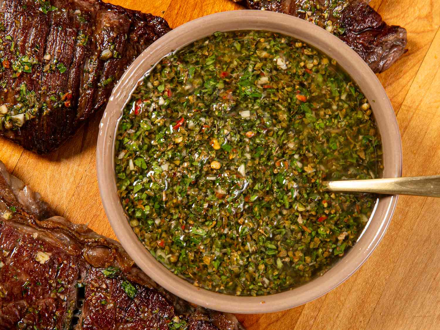 Overhead view of chimichurri sauce in a bowl between two pieces of steaks. 