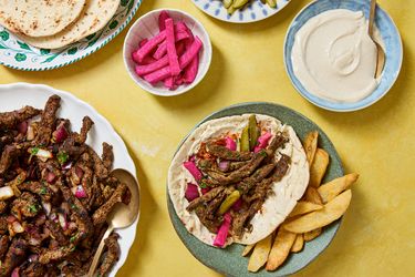 Beef shawarma wrap with accompaniments including pickles tahini sauce and pita bread on a table