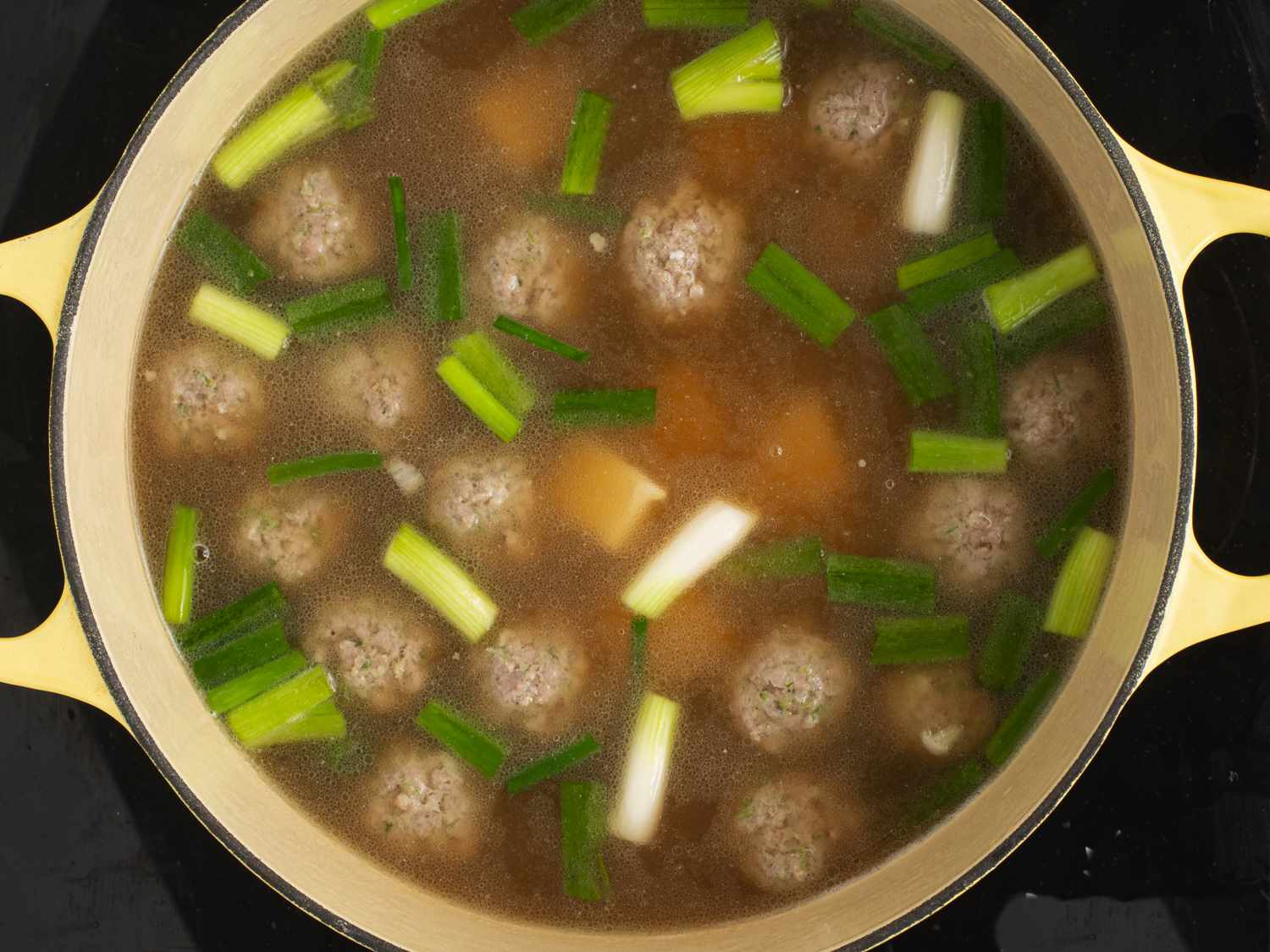 The Dutch oven holding the soup, meatballs, tofu, and 1-inch length of scallions.
