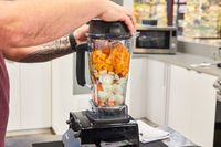 Hands putting the lid on a Vitamix 5200 Professional-Grade Blender filled with fruit and vegetables