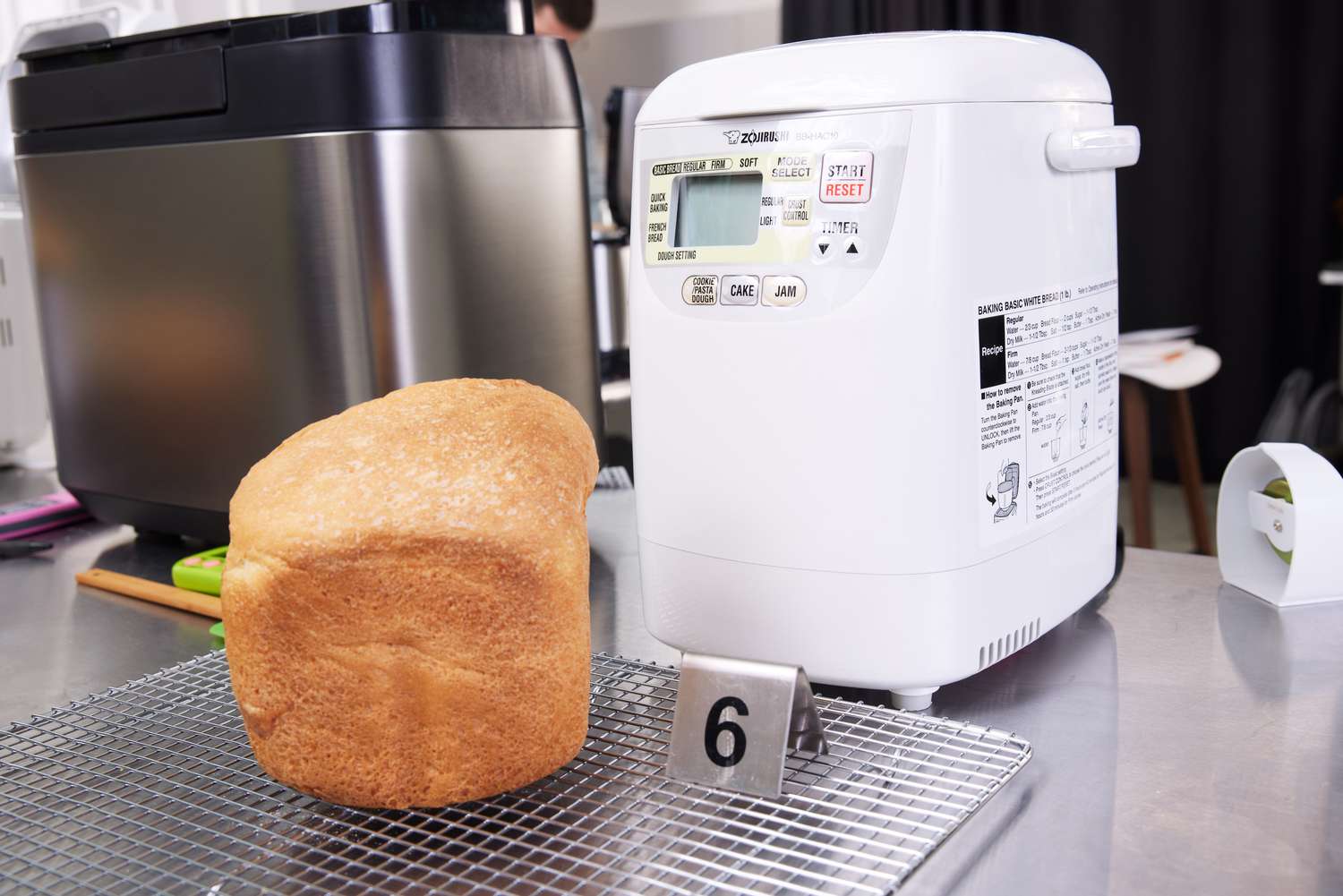 Baked bread on metal rack next to Zojirushi BB-HAC10 Home Bakery Mini Breadmaker