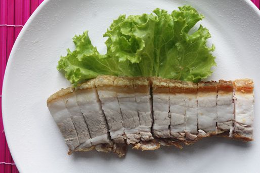 A closeup of a thick slice of Chinese crispy roast pork belly that's been cut into 1/2-inch lardons and arranged on a lettuce-lined plate.