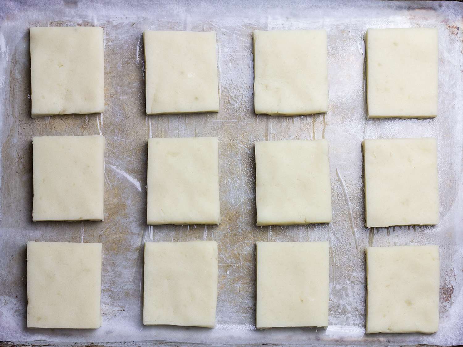 Potato mochi dough cut into identical squares on a baking sheet
