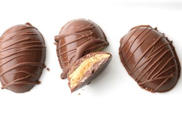 Overhead view of several peanut butter cup eggs, decoratively drizzled with extra chocolate. One of the eggs has been broken in half and upturned to reveal the interior.
