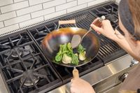 A person cooks bok choi in the Joyce Chen Carbon Steel Wok