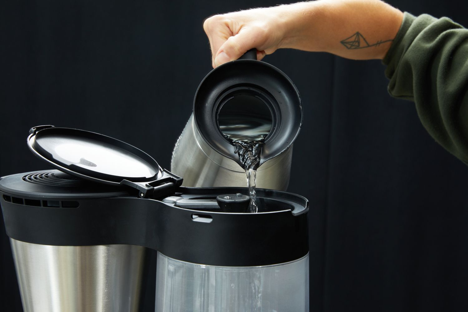 A person pouring water into a coffee maker's water reservoir. 