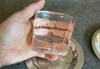 A hand holding a clear squareshaped ice cube over a reflective surface