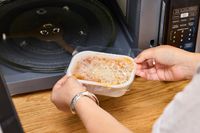 Two hands placing a meal into the Farberware Countertop Compact Microwave (FMWO11AHTBKB) 