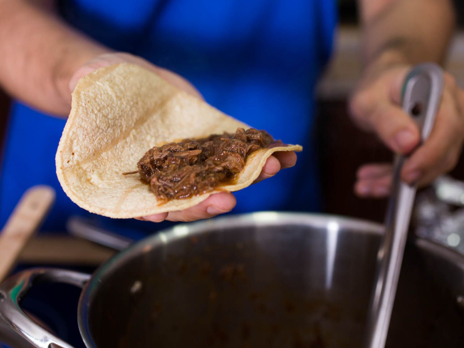 A hand holding corn tortilla topped with braised beef