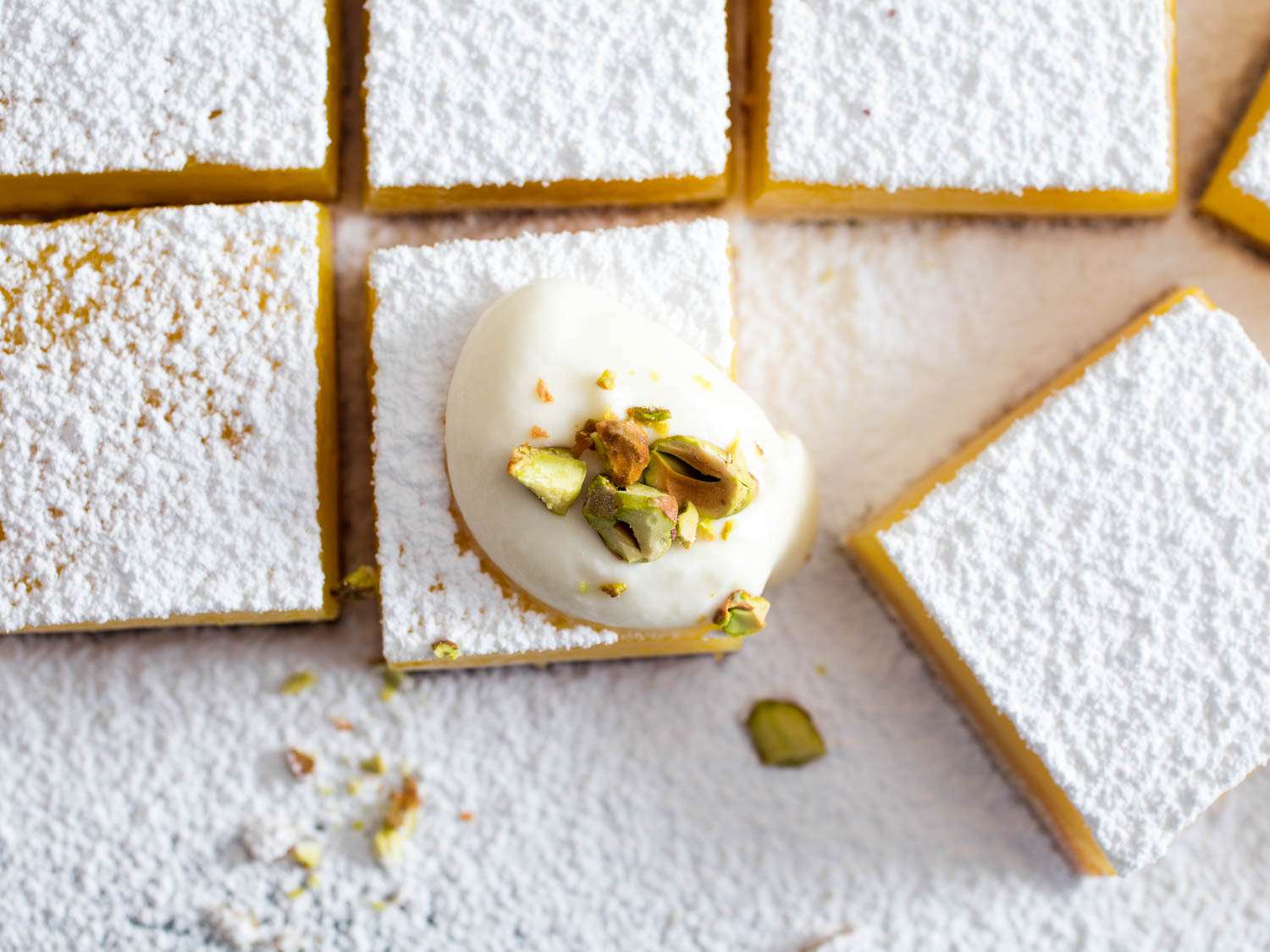 Sliced lemon bars topped with powdered sugar, lemon chantilly, and chopped pistachios.