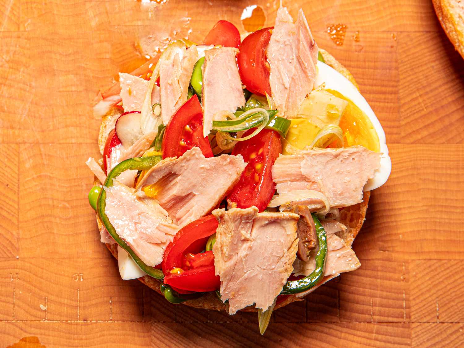 Open sandwich topped with tuna tomatoes peppers and onions on a wooden surface