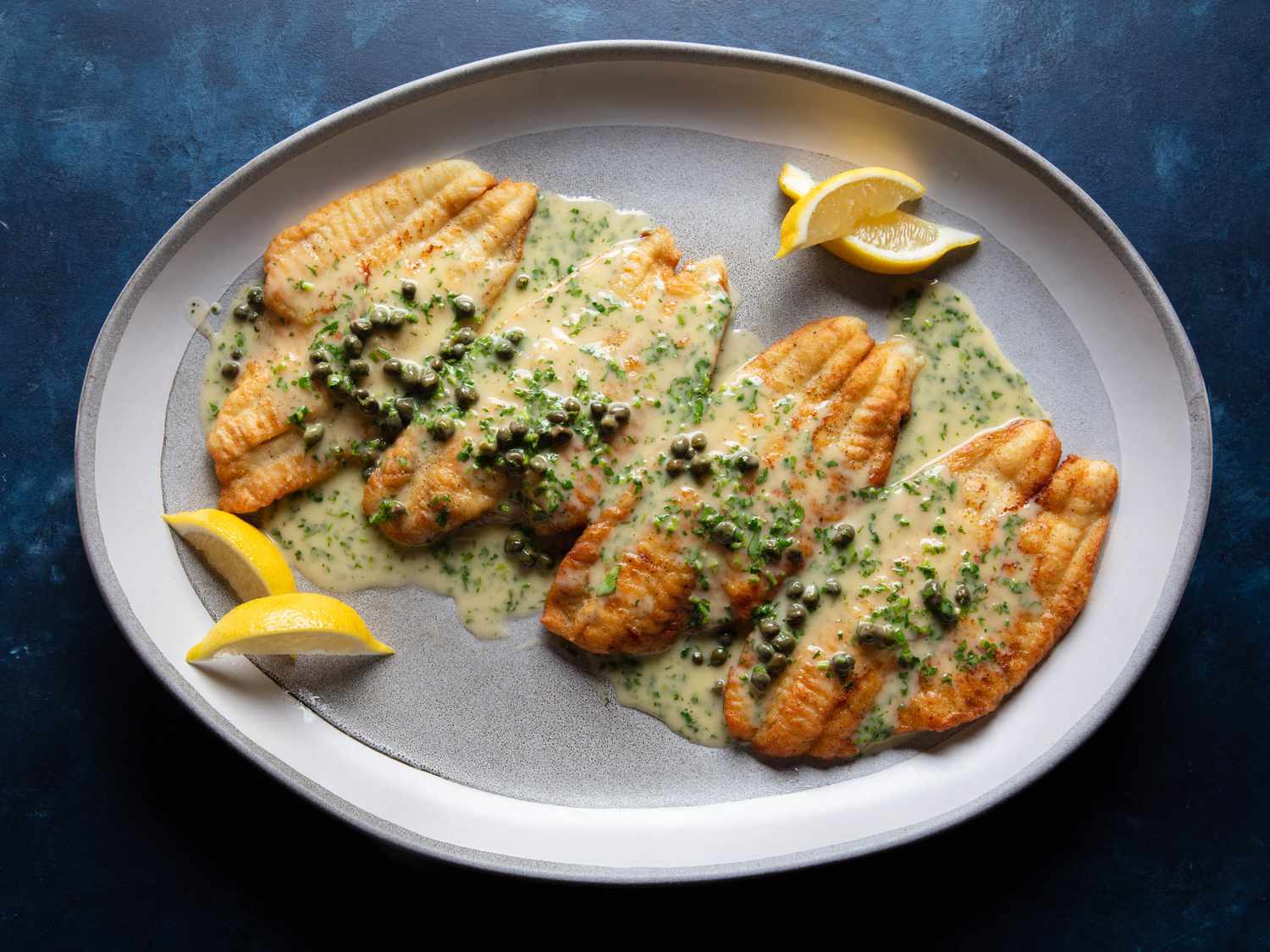 Four browned fish fillets sit on a large platter with the sauce poured on top and all around.