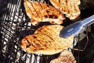 Chicken breasts cooking on a grill with tongs holding one piece
