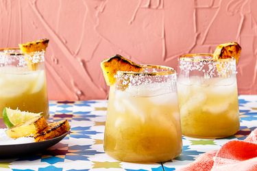 Three glasses of margarita with grilled pineapple garnishes on a colorful table
