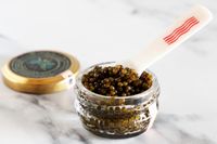 An open jar of Caviar Co kaluga hybrid caviar with a mother-of-pearl spoon inside