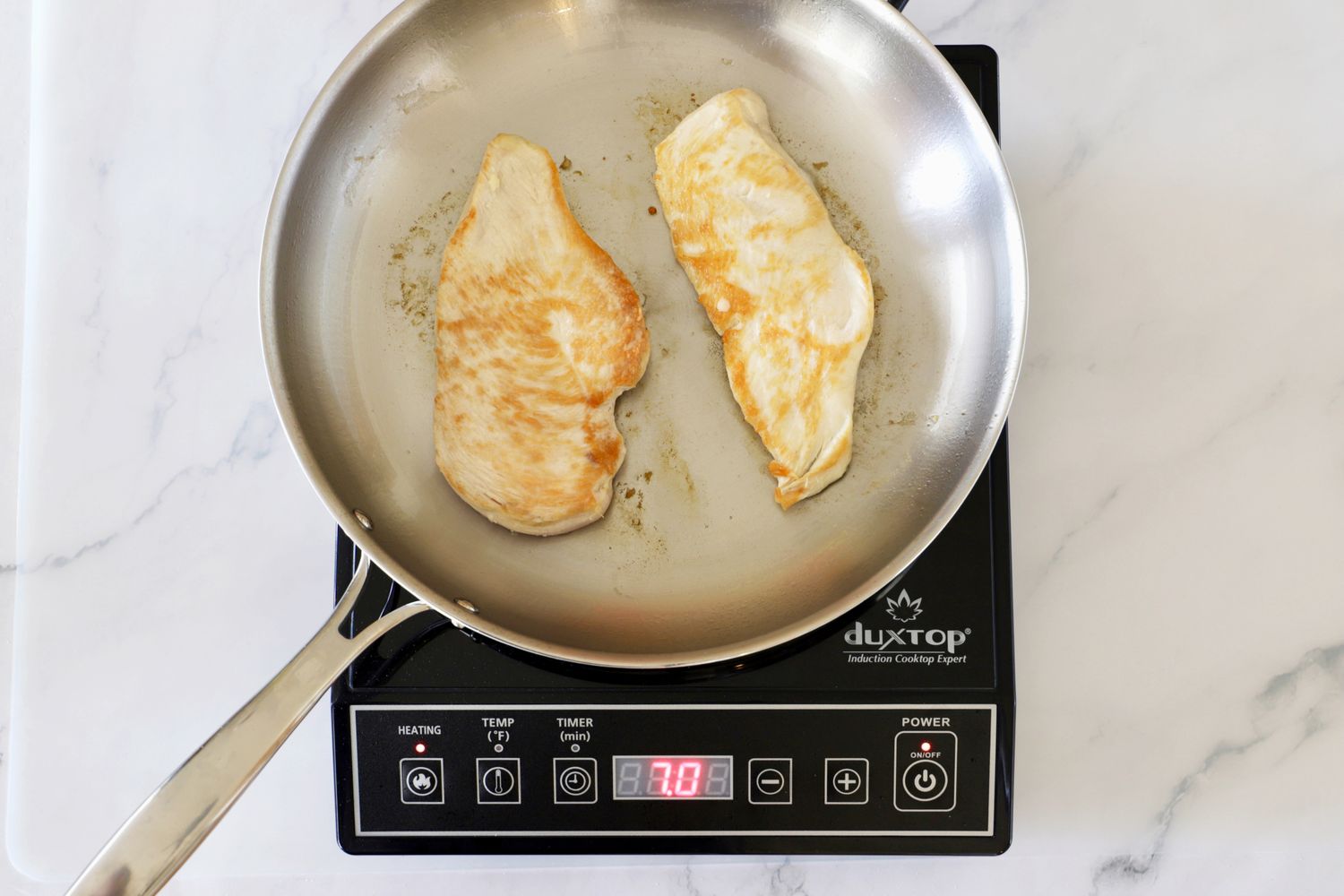 Two chicken breast fillets being cooked in a frying pan on a Duxtop portable induction cooktop