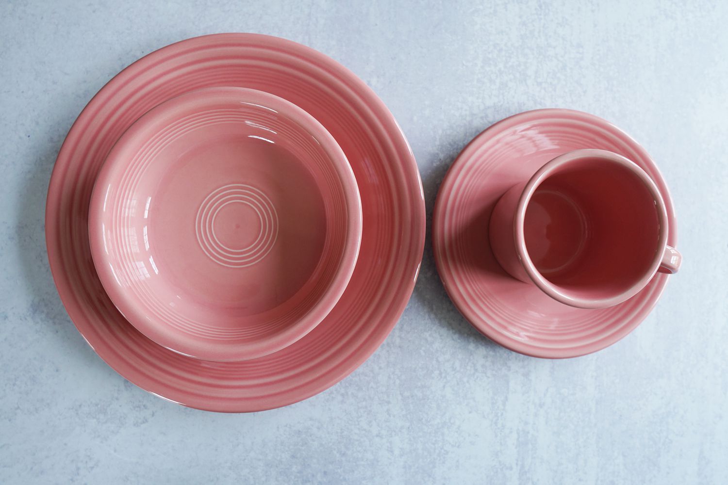 Two pink plates, a pink bowl, and a pink mug on a grey surface