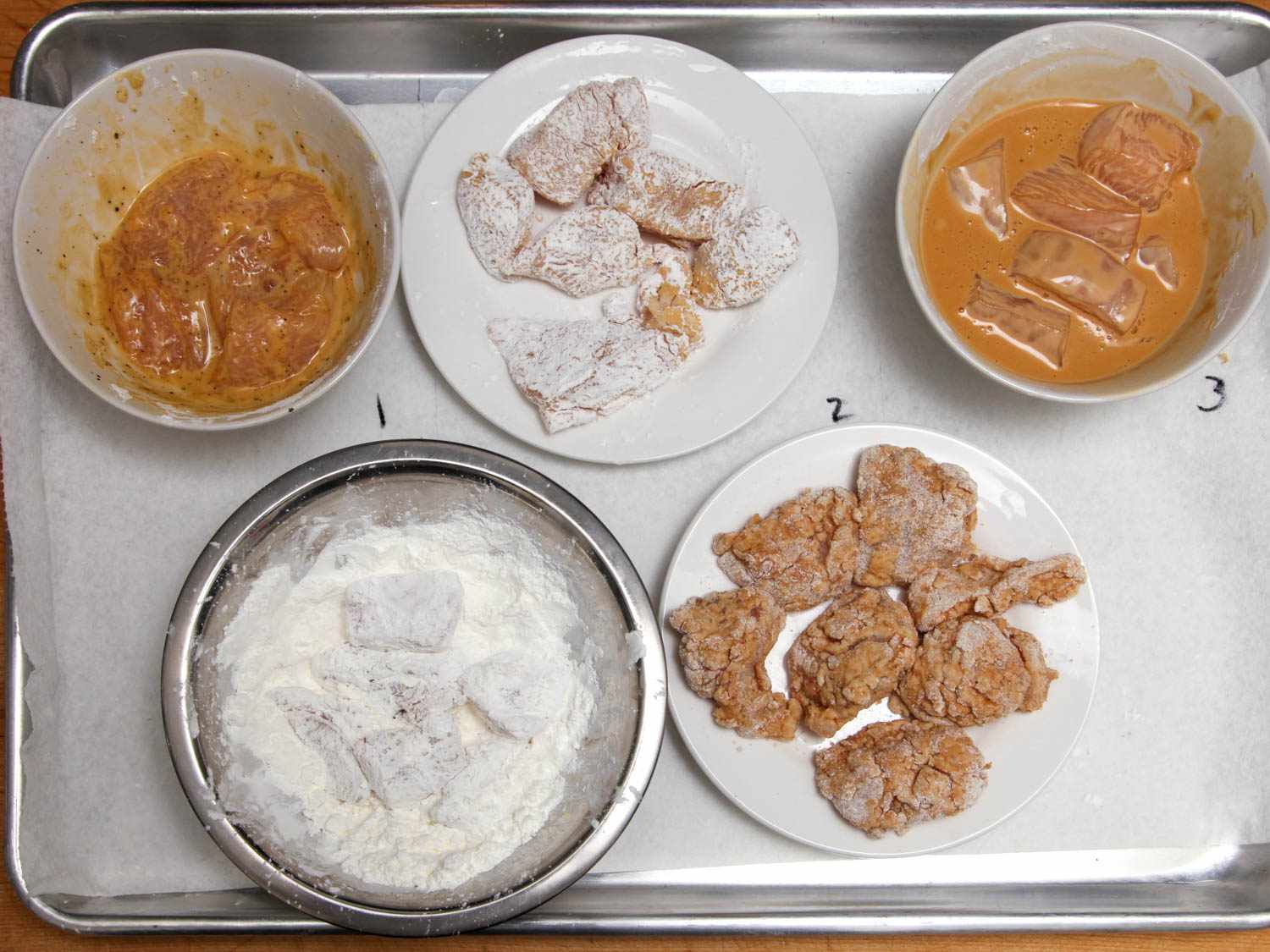 Boneless chicken thighs cut into pieces and in five different bowls with five different breadings or batters.