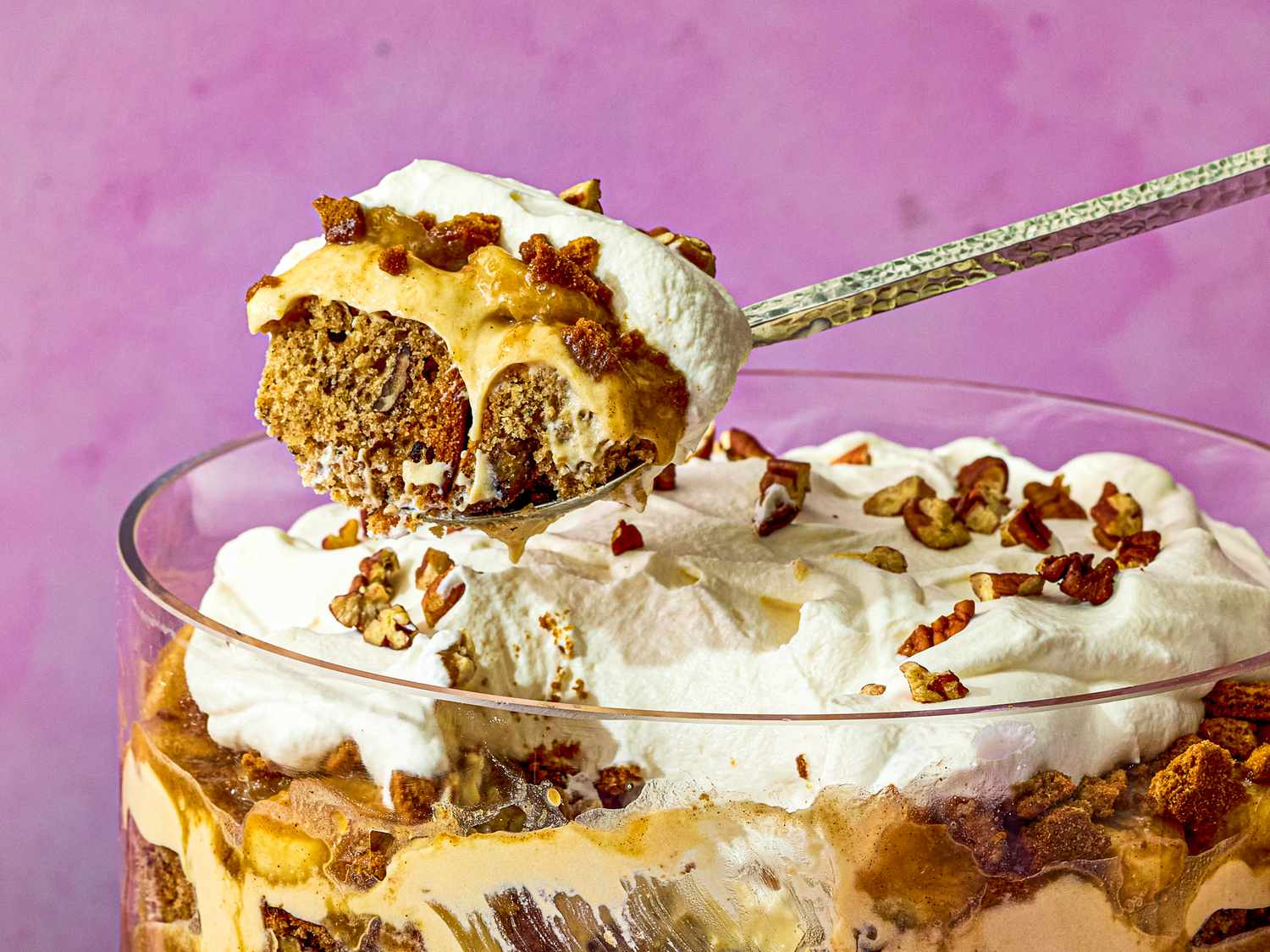 Banana bread trifle with whipped cream and pecans in a glass bowl spoon scooping a portion