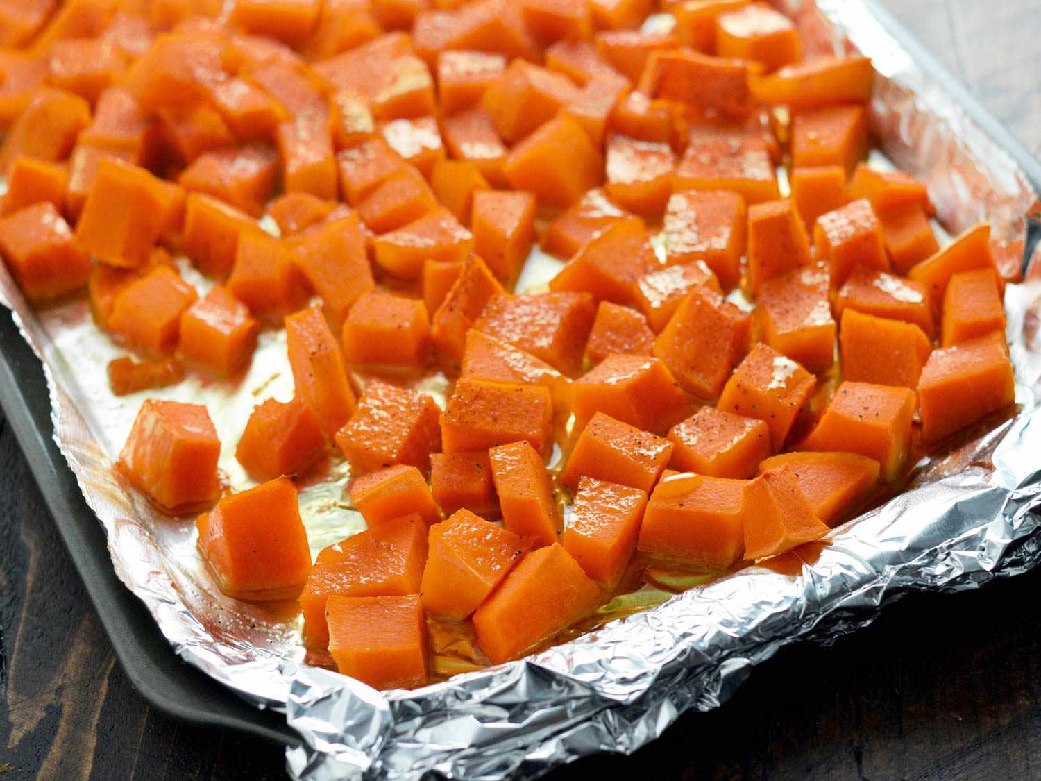 Butternut squash cubes tossed in oil in a foil-lined baking sheet, about to be roasted.