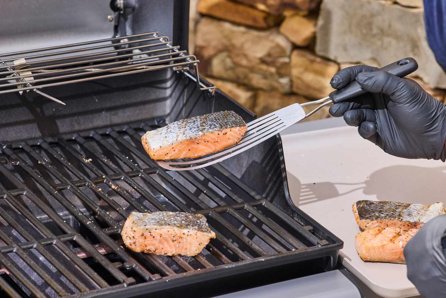A gloved hand lifting salmon off of the Weber Spirit E-310 Gas Grill with a spatula