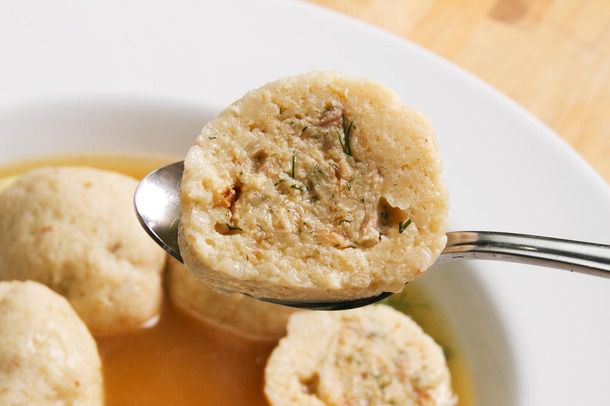 A spoon lifting a chicken-stuffed matzo ball out of a bowl, with other matzo balls and broth visible in the background