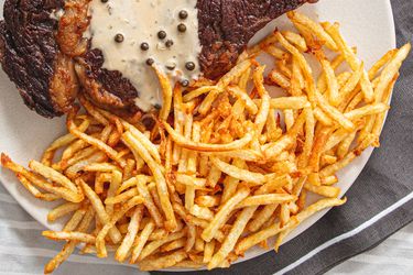 A steak with pepper sauce next to a serving of thincut fries on a plate